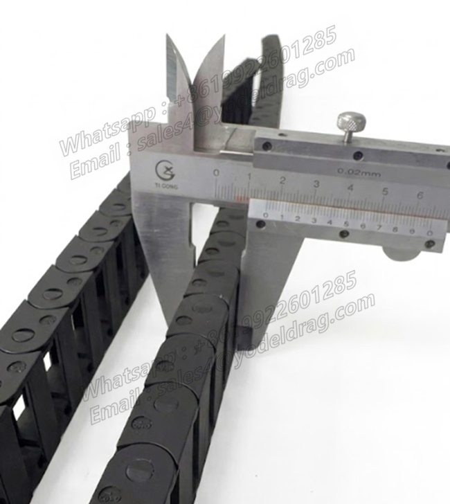 Calipers measuring the outer height of a black PA66 bridge-type miniature cable carrier for quality verification