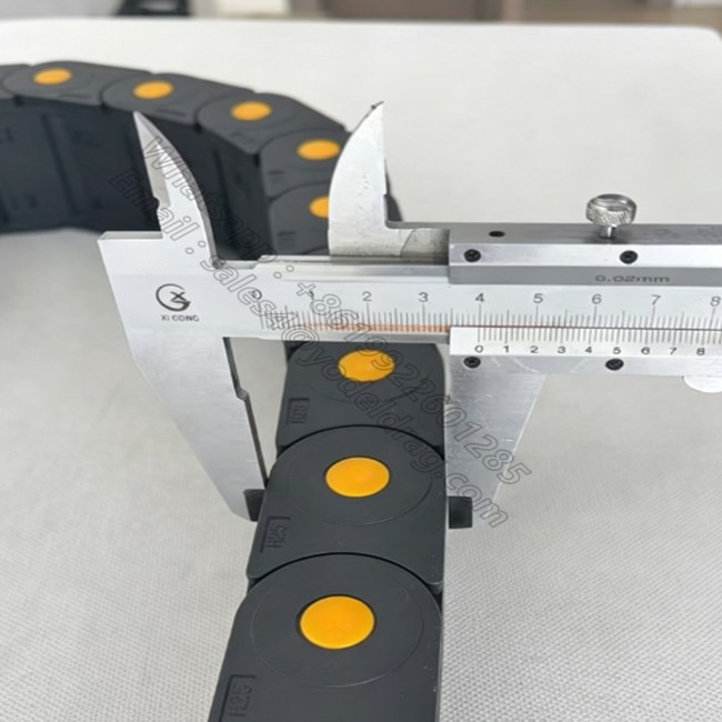Measuring the outer height and link pitch of an enclosed CNC cable chain with a vernier caliper.
